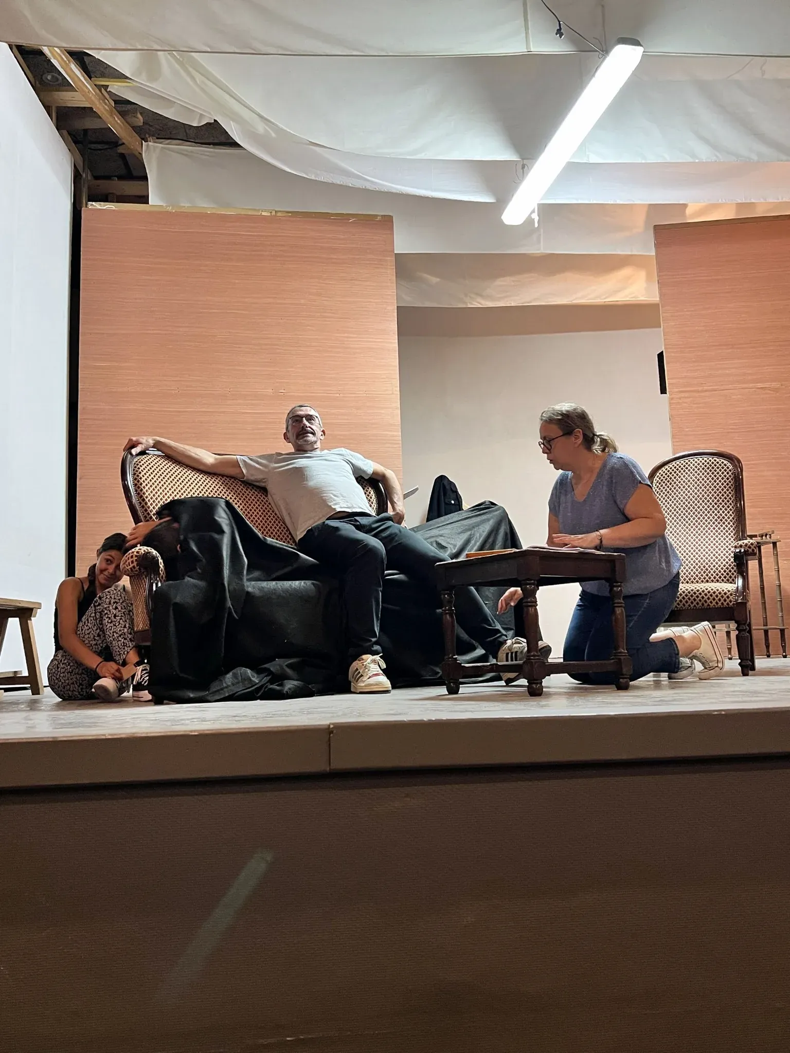 Répétition dans le décor du salon : un comédien affalé sur une banquette, une comédienne à genoux près de la table basse