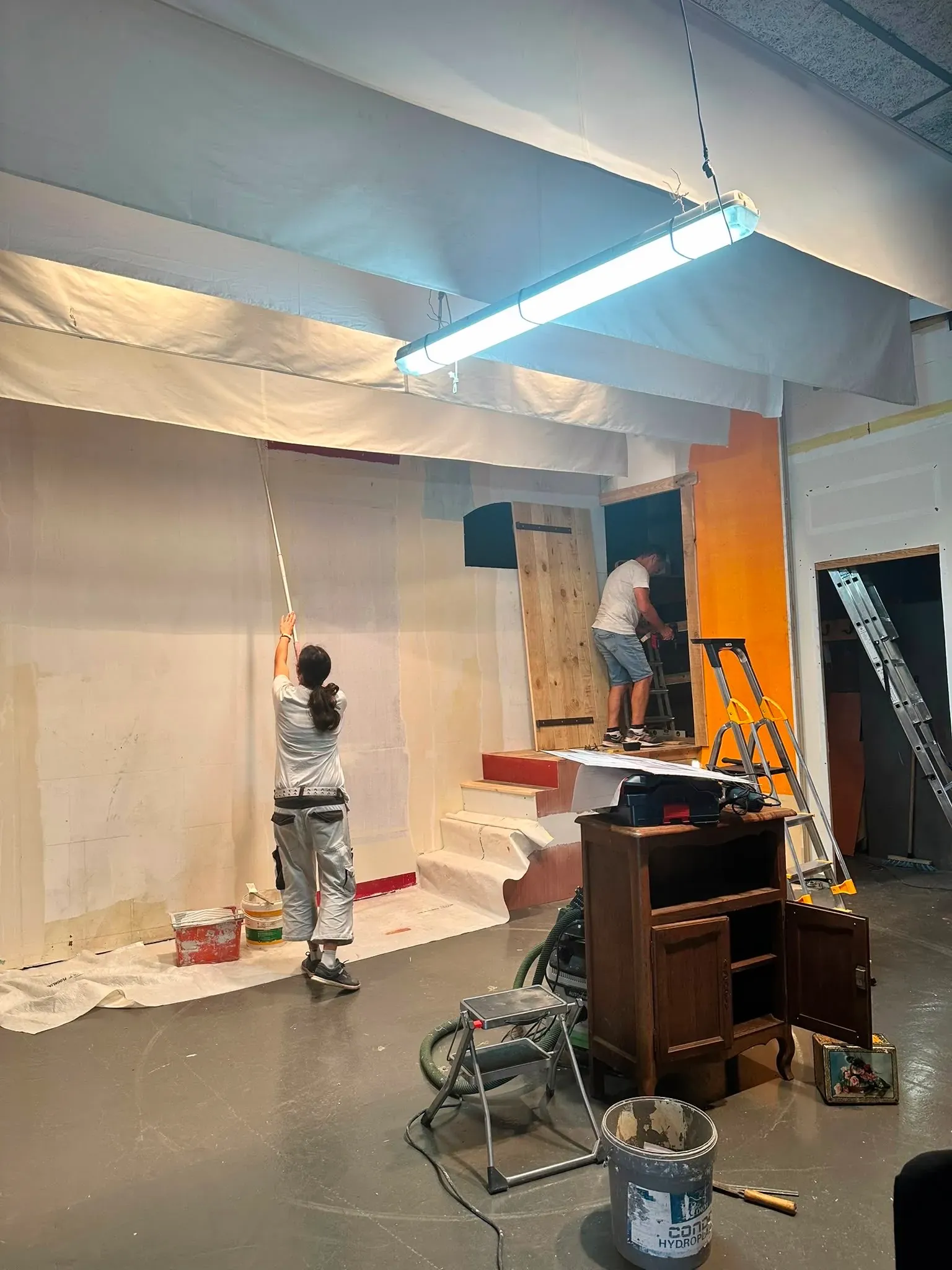 L'équipe décor au travail : peinture d'un mur au rouleau et montage d'une porte en bois