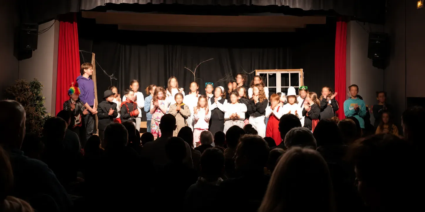 Salut final d'un spectacle de l'atelier : une trentaine de jeunes comédiens en costume applaudissent sur scène, face au public dans la pénombre